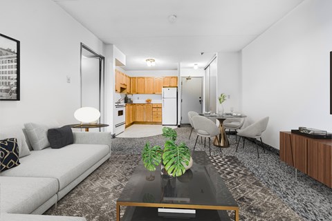 A modern living room with a grey sofa, a glass coffee table, and a dining area in the background.