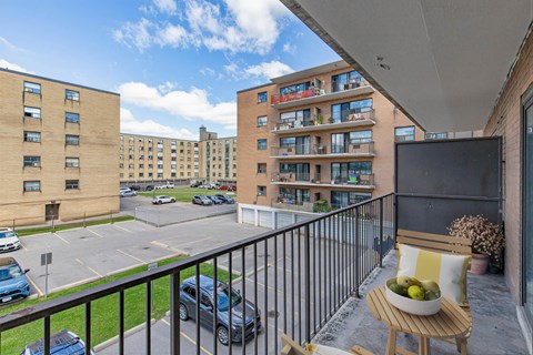 A balcony with a table and chairs overlooks a parking lot and buildings.