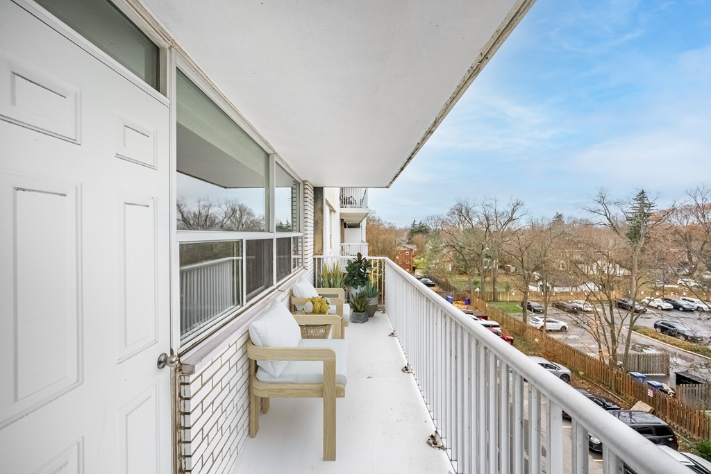 A balcony with a chair and table is overlooking a parking lot.