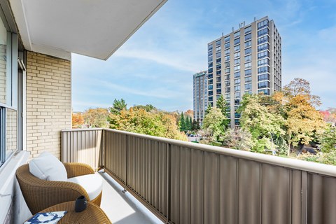 A balcony with a chair and a table overlooks a cityscape.