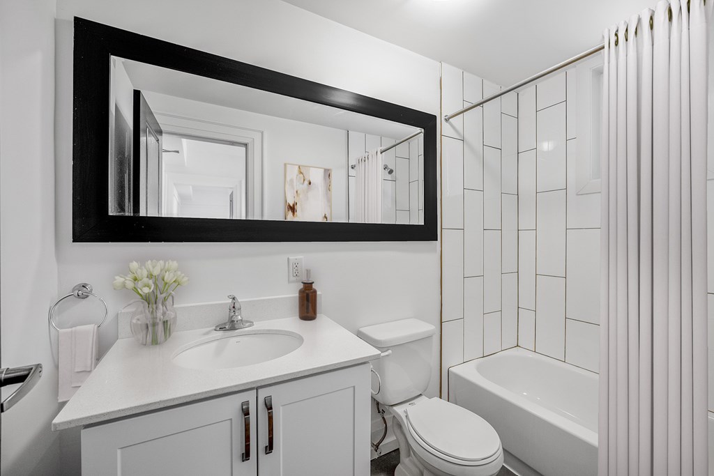 A white bathroom with a black framed mirror above a sink.