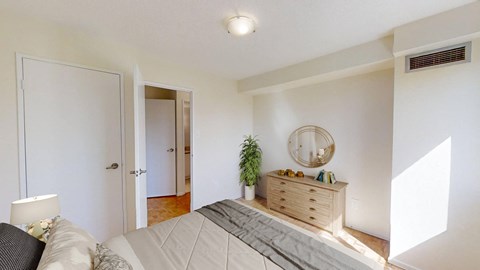 A bedroom with a bed, nightstand, and a plant.