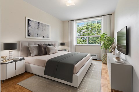 A bedroom with a large bed, a nightstand, and a window with a view of trees.