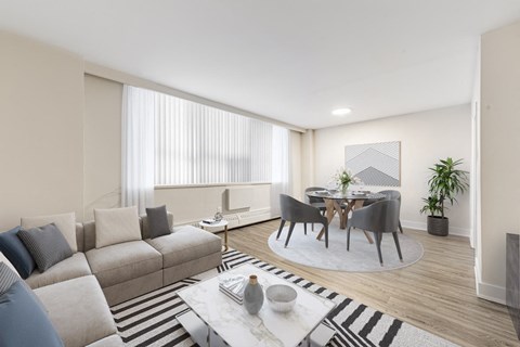 A modern living room with a grey sofa, a coffee table, and a dining table set up.