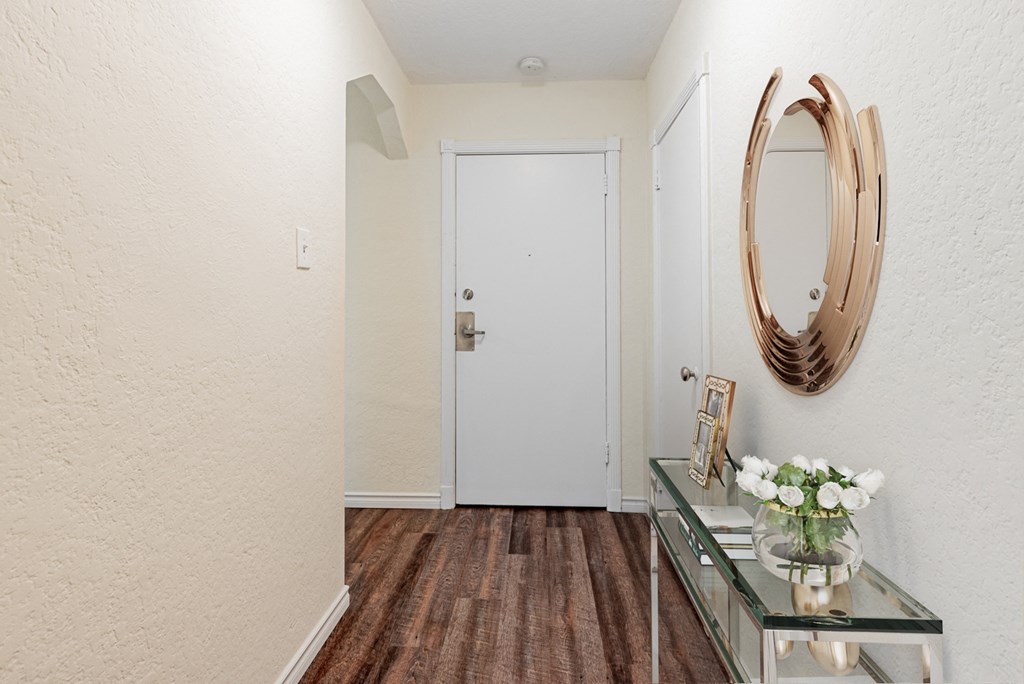 A hallway with a white door, a mirror, and a table with flowers.