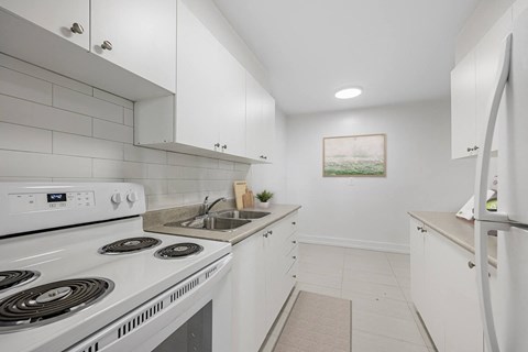 A white kitchen with a stove, sink, and refrigerator.