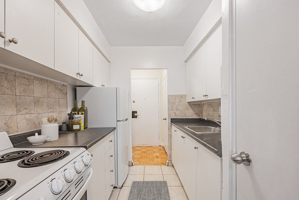 A kitchen with a white stove top oven and white cabinets.