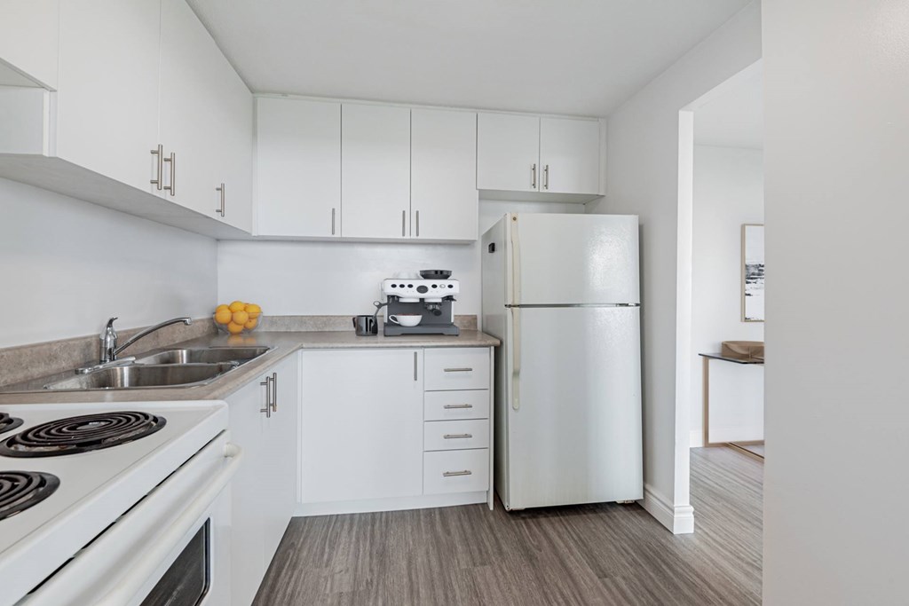 A white kitchen with a refrigerator, sink, and stove.