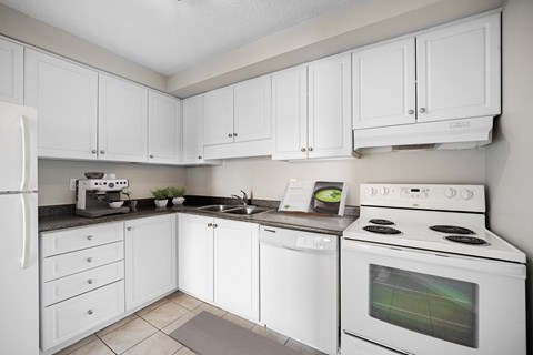 A white kitchen with a refrigerator, microwave, oven, and sink.