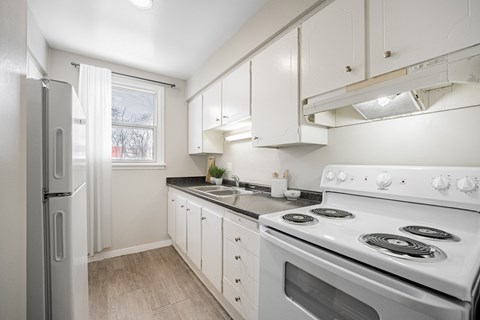 A white kitchen with a stove, sink, and refrigerator.