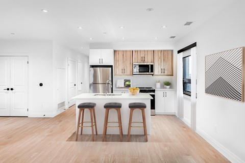 A kitchen with white walls and wooden floors has a white island with three stools.