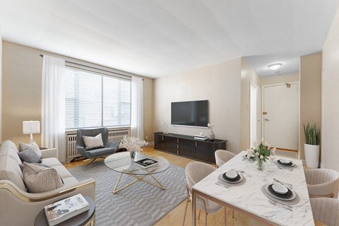 A modern living room with a grey sofa, a white coffee table, a TV, and a dining table set for two.