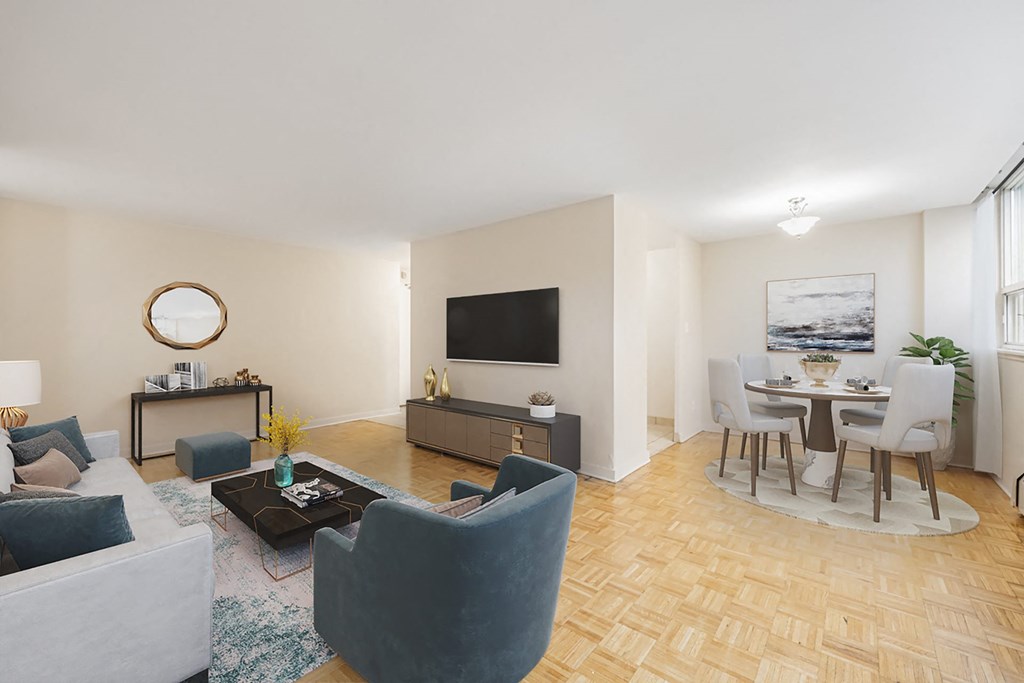 A living room with a grey couch, a blue armchair, a coffee table, a television, and a dining table with chairs.