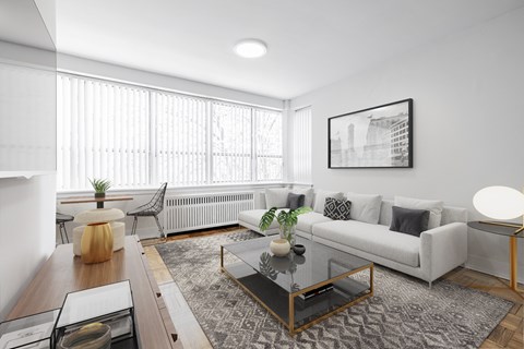 A modern living room with a white couch, a glass coffee table, and a large window with blinds.