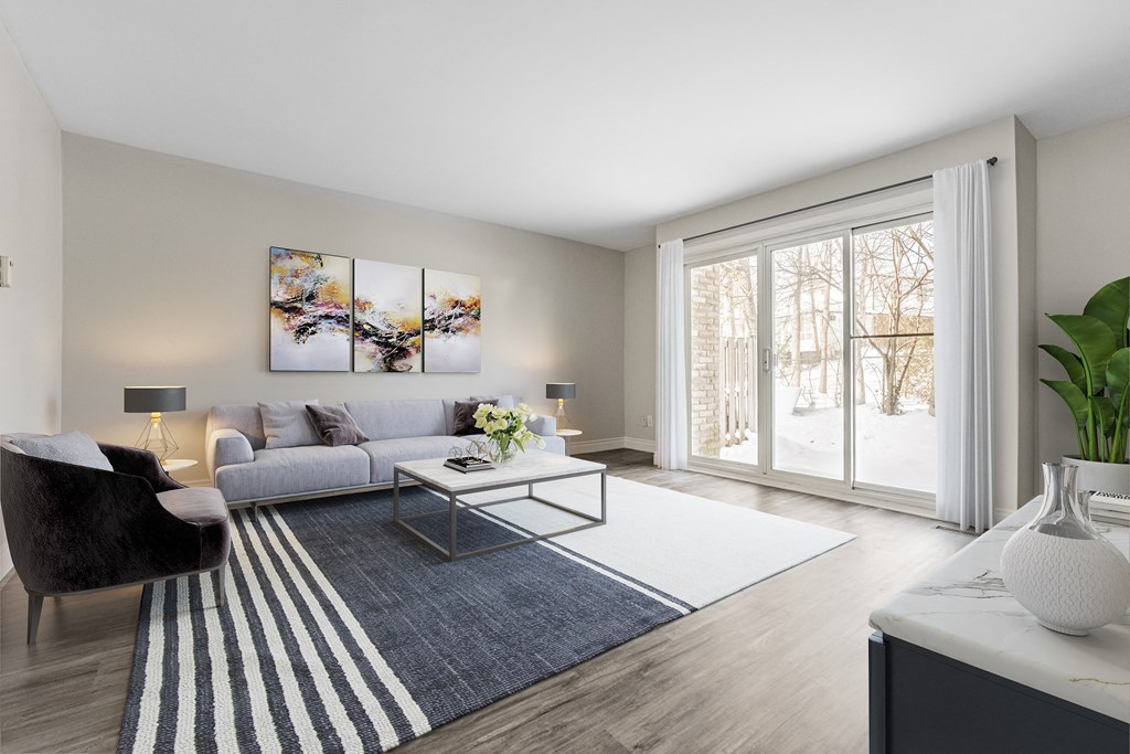 A modern living room with a grey sofa, a black chair, a coffee table, and a large window.