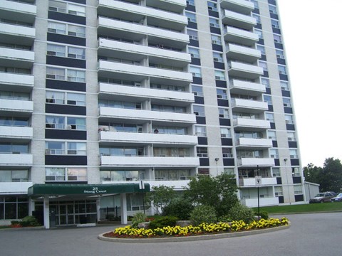 A large white building with a green awning and a flower bed in front.