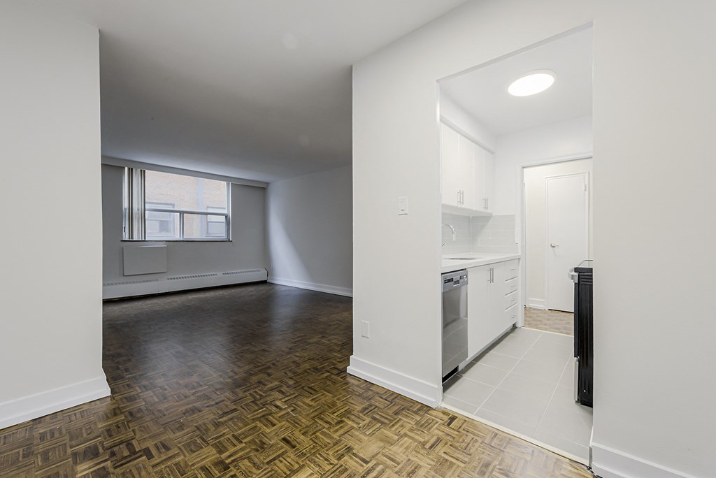 an empty living room and kitchen with white walls and wood flooring