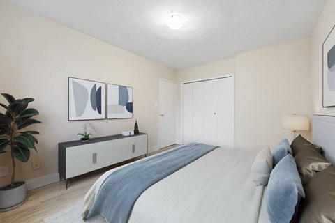 A bedroom with a bed, a plant, and two framed pictures on the wall.