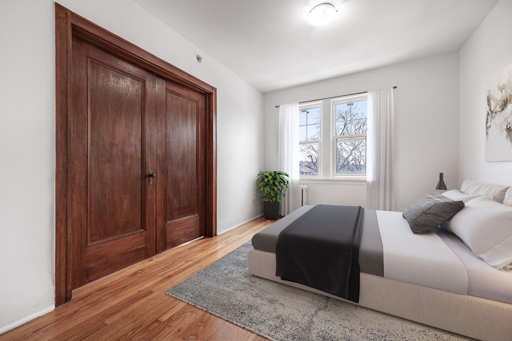 A bedroom with a bed, a rug, a plant, and a wooden door.
