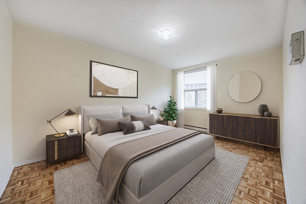 A bedroom with a large bed, a nightstand with a lamp, and a plant on the windowsill.