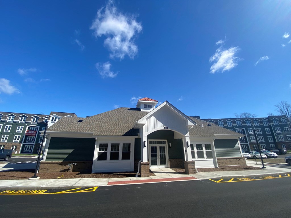 A building with a white door and a red roof is in front of a row of apartment buildings.