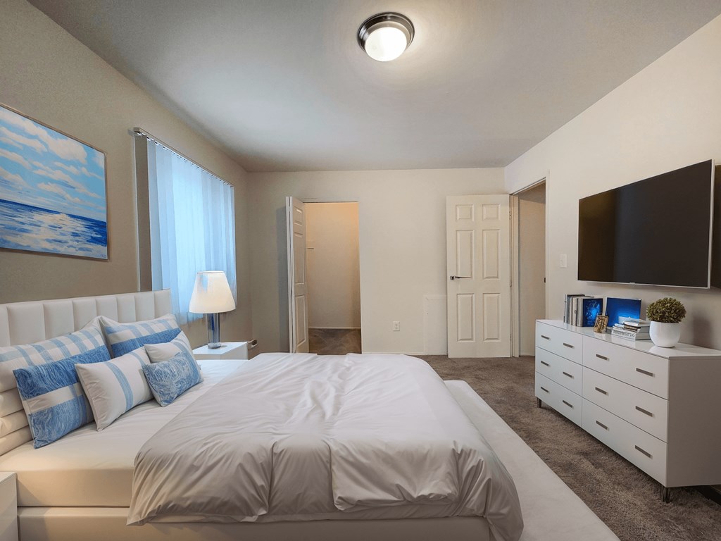 A bedroom with a large bed, a dresser, and a painting on the wall.