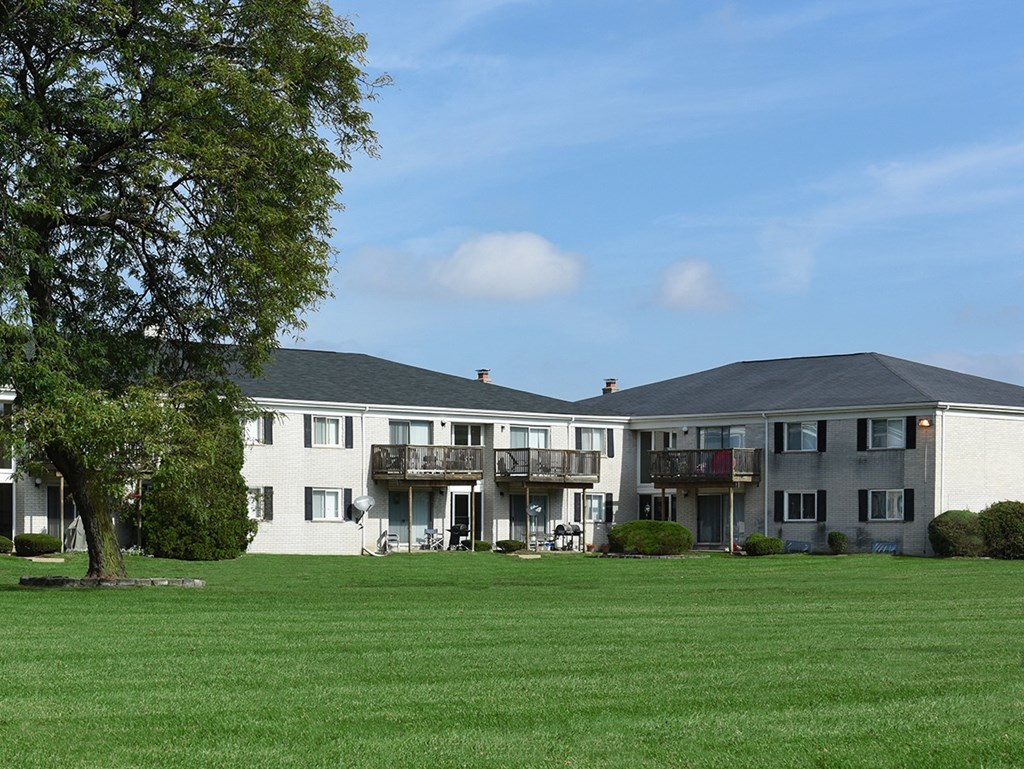 A large grassy field in front of a building with a tree on the left.