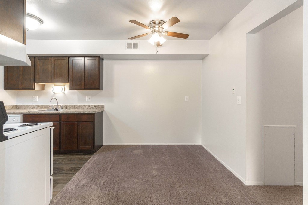 an empty kitchen with a ceiling fan and an empty room with a kitchen counter top
