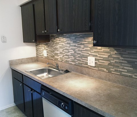 A kitchen with a stone backsplash and dark cabinets.