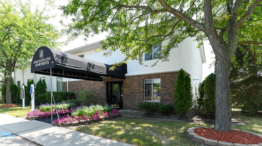 A building with a sign that says "Bourbon Lane Apartments" is surrounded by trees and flowers.