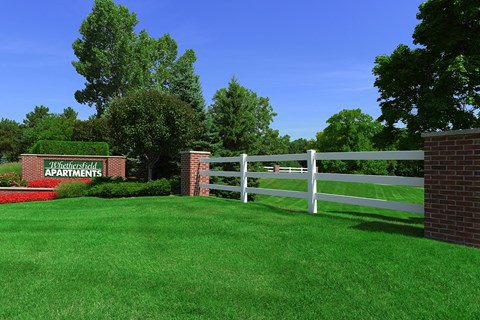 A sign that says "Whitfield Apartments" is in front of a white fence.