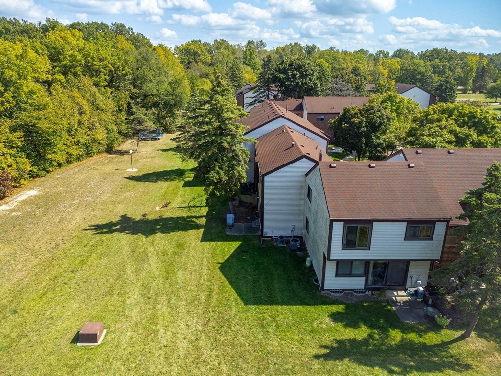 A house with a brown roof is surrounded by a green lawn and trees.