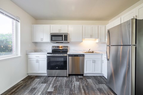 A kitchen with white cabinets and a wood floor.