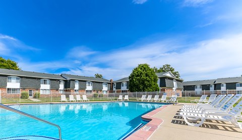A swimming pool surrounded by lounge chairs and apartment buildings.
