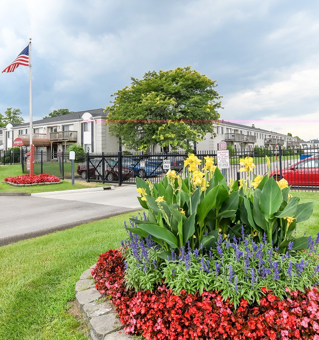 A flower bed with red, pink, and purple flowers in front of a building with a flag.