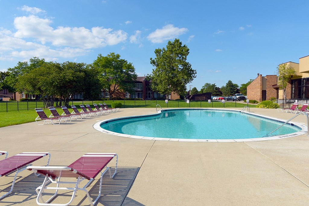 A pool surrounded by trees and chairs.