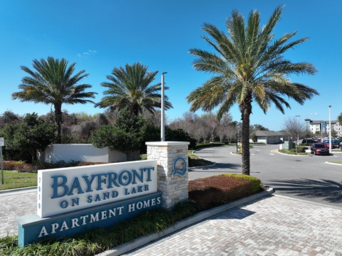 A sign for Bayfront on Sand Lake Apartment Homes is in front of some palm trees.