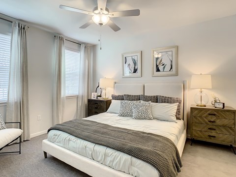 A bedroom with a large bed, a ceiling fan, and two nightstands.
