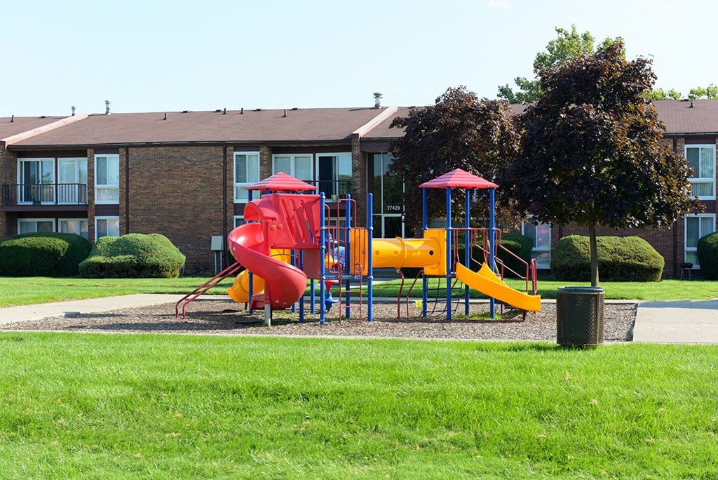 A playground with a red slide and a yellow slide in front of a building.