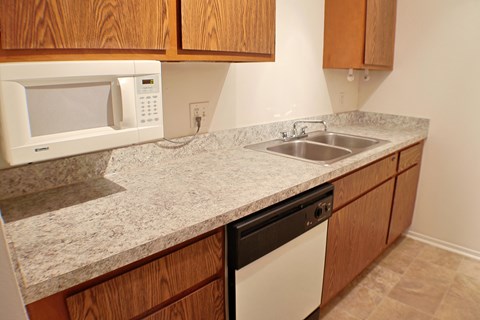 A kitchen with a white microwave, sink, and dishwasher.