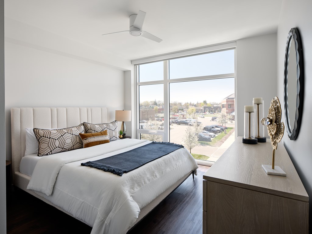 A bedroom with a large bed and a view of a parking lot outside the window.