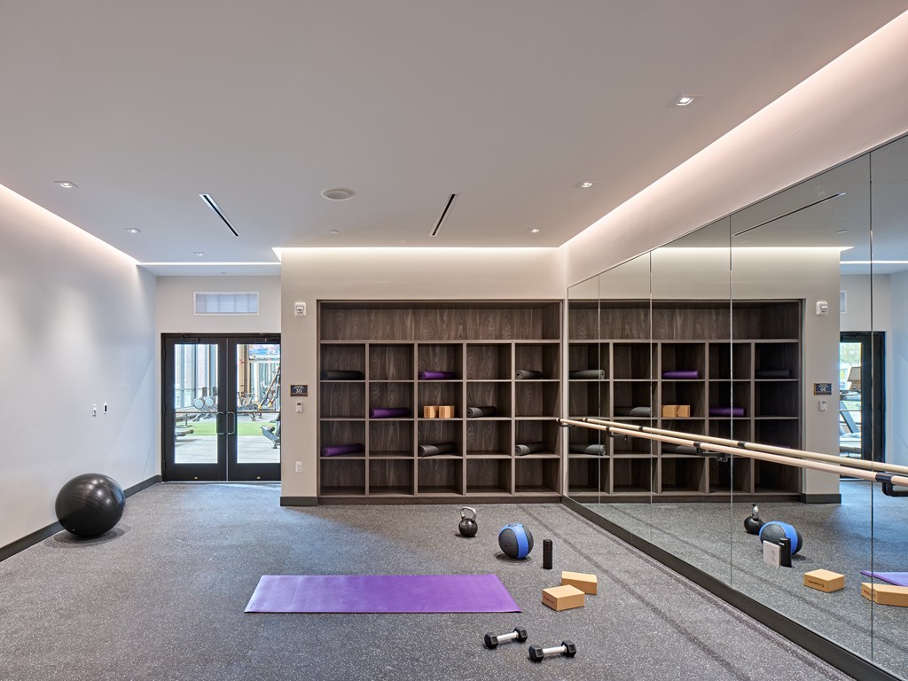 A gym with a purple mat, a black ball, and a glass wall.