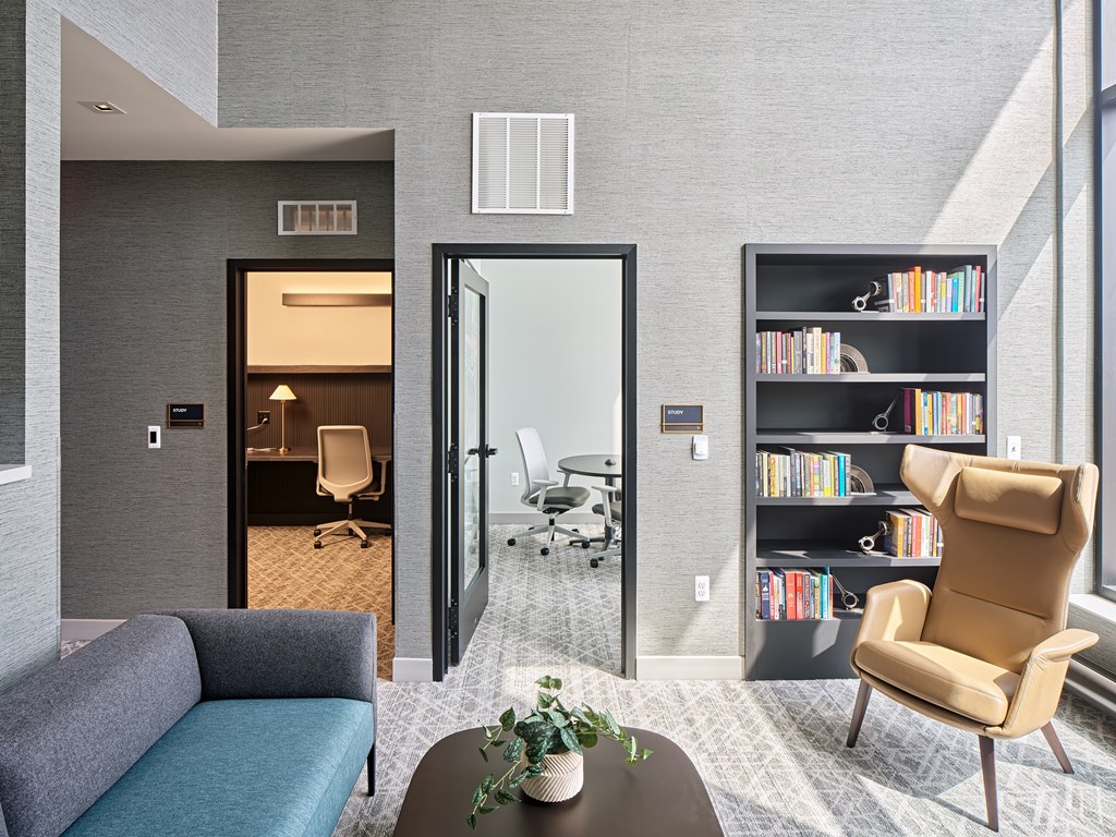 A modern living room with a grey couch, a brown chair, and a bookshelf filled with books.