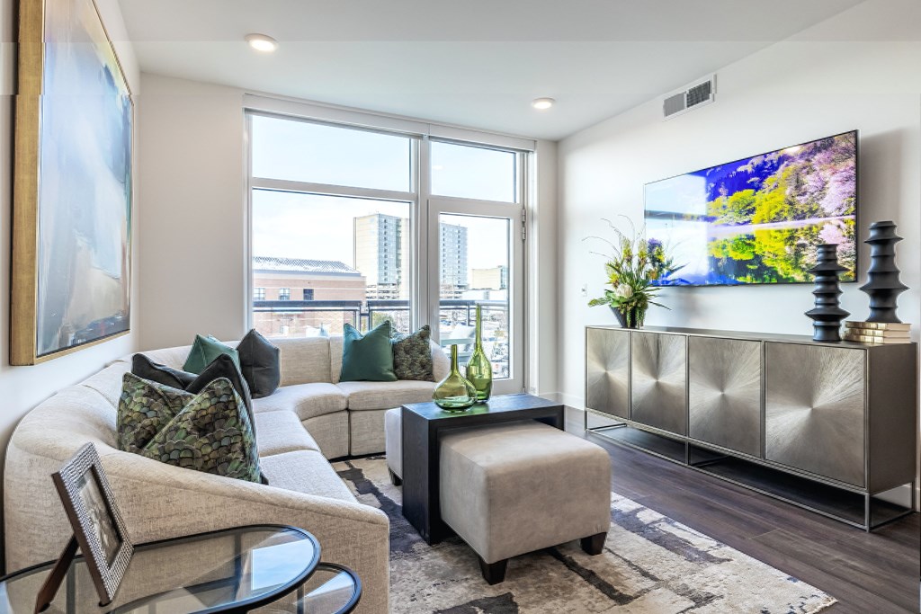A living room with a large window, a sofa, a chair, a coffee table, and a TV.