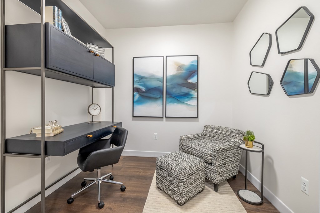 A room with a grey chair, a desk, and a painting on the wall.