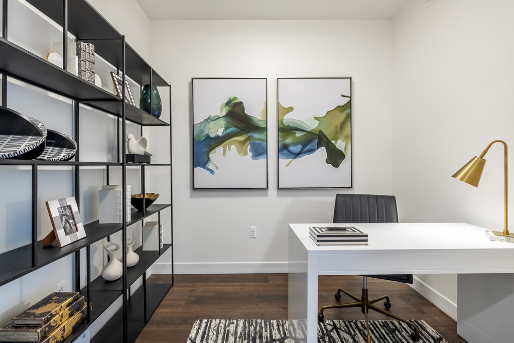 A room with a white desk, black chairs, and two framed artworks on the wall.