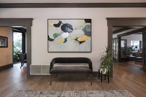 A large abstract painting hangs on a wall above a grey bench in a spacious room.