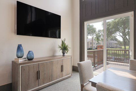 A black TV is mounted on a wall above a wooden cabinet with two doors and a shelf with three blue vases and a green plant.