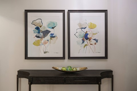 Two framed artworks hang on a wall above a dark desk with a green bowl on it.