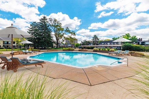 A large outdoor swimming pool surrounded by a concrete patio and deck chairs.